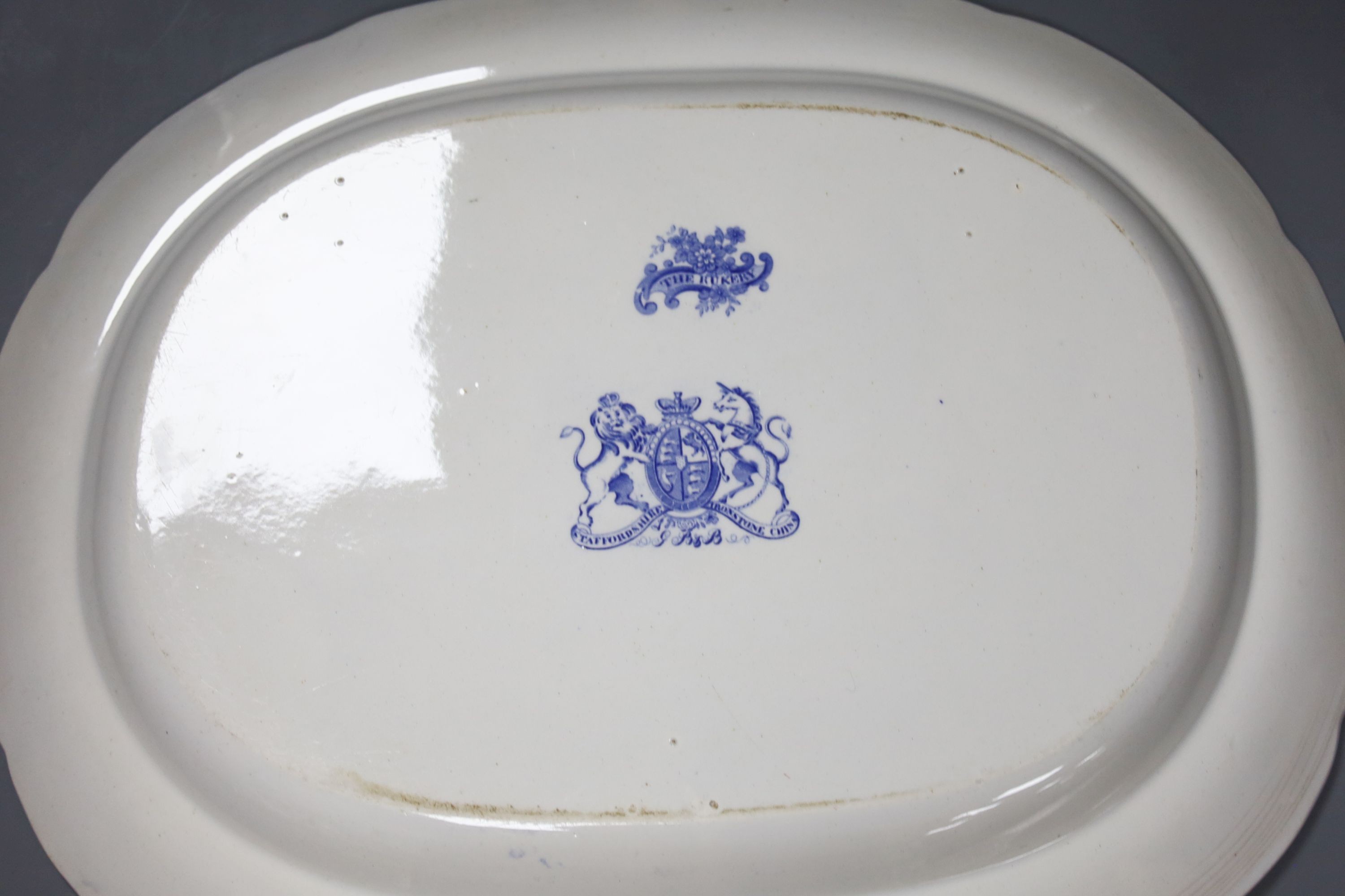 A late 19th century Staffordshire blue and white transfer-printed oval meat dish, ‘The Rokery’, depicting a country house with lake and figures, W 44cm and an octagonal 'Flora' creamware soup tureen with ladle and stand